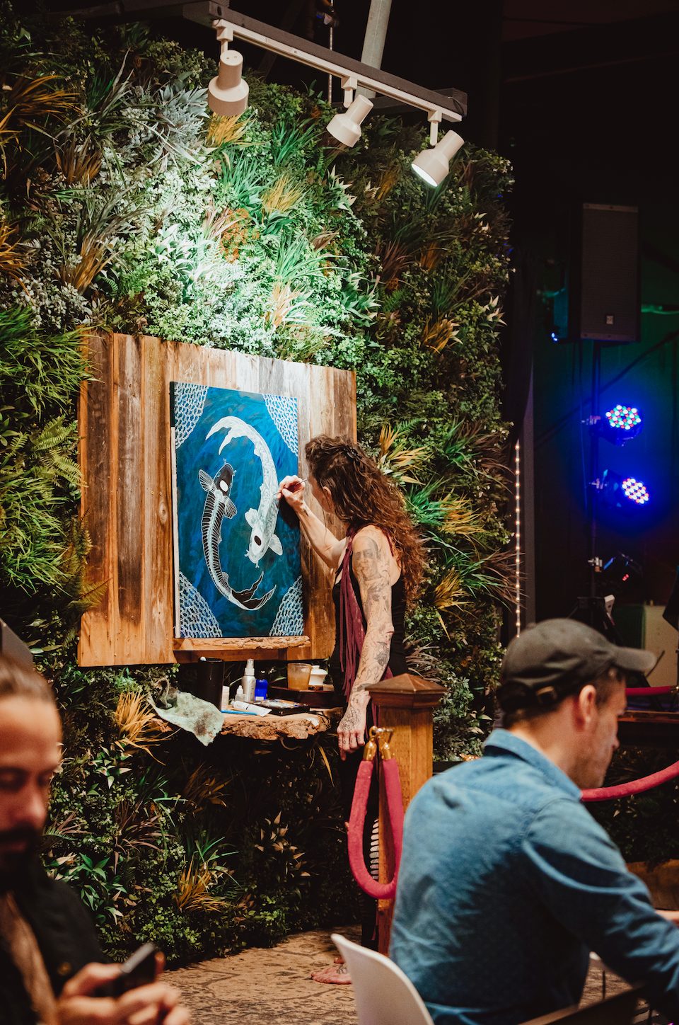An artist painting live on canvas beside a wall of greenery