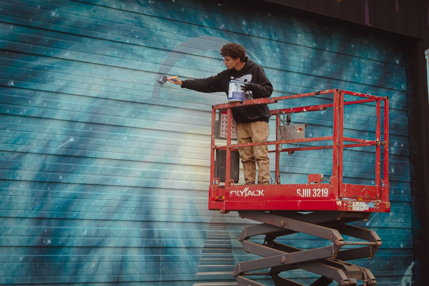 An artist on a lift painting a large mural in the early days of The Haven
